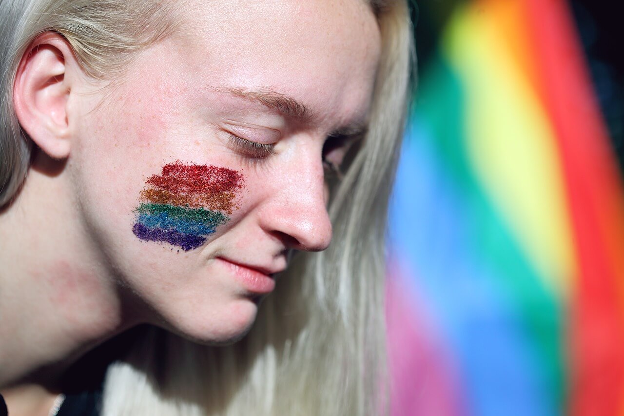 Image of a woman with a rainbow on her cheek and a pride flag in the background
